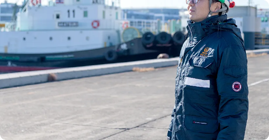 港で作業服を着た人が船の前に立っている。